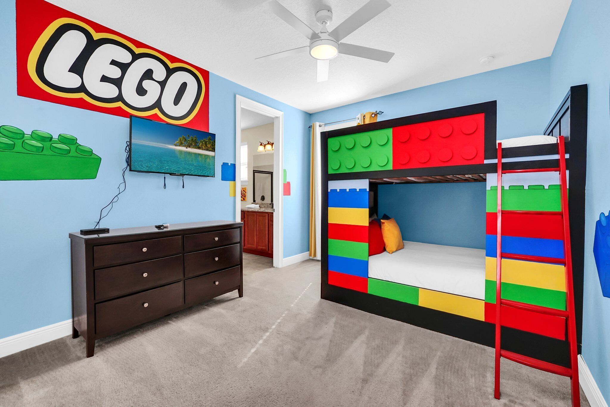 A room with a LEGO-themed bed, a dark wooden dresser, and a TV on the wall.