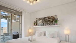 A modern bedroom with a large bed, two bedside tables with lamps, a decorative wall piece, and a sliding glass door leading to a balcony. - Residencial Koma by Interhome (Torrevieja)