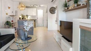A modern living room with a glass coffee table, a grey sofa, a TV, and a fireplace. - Residencial Koma by Interhome (Torrevieja)