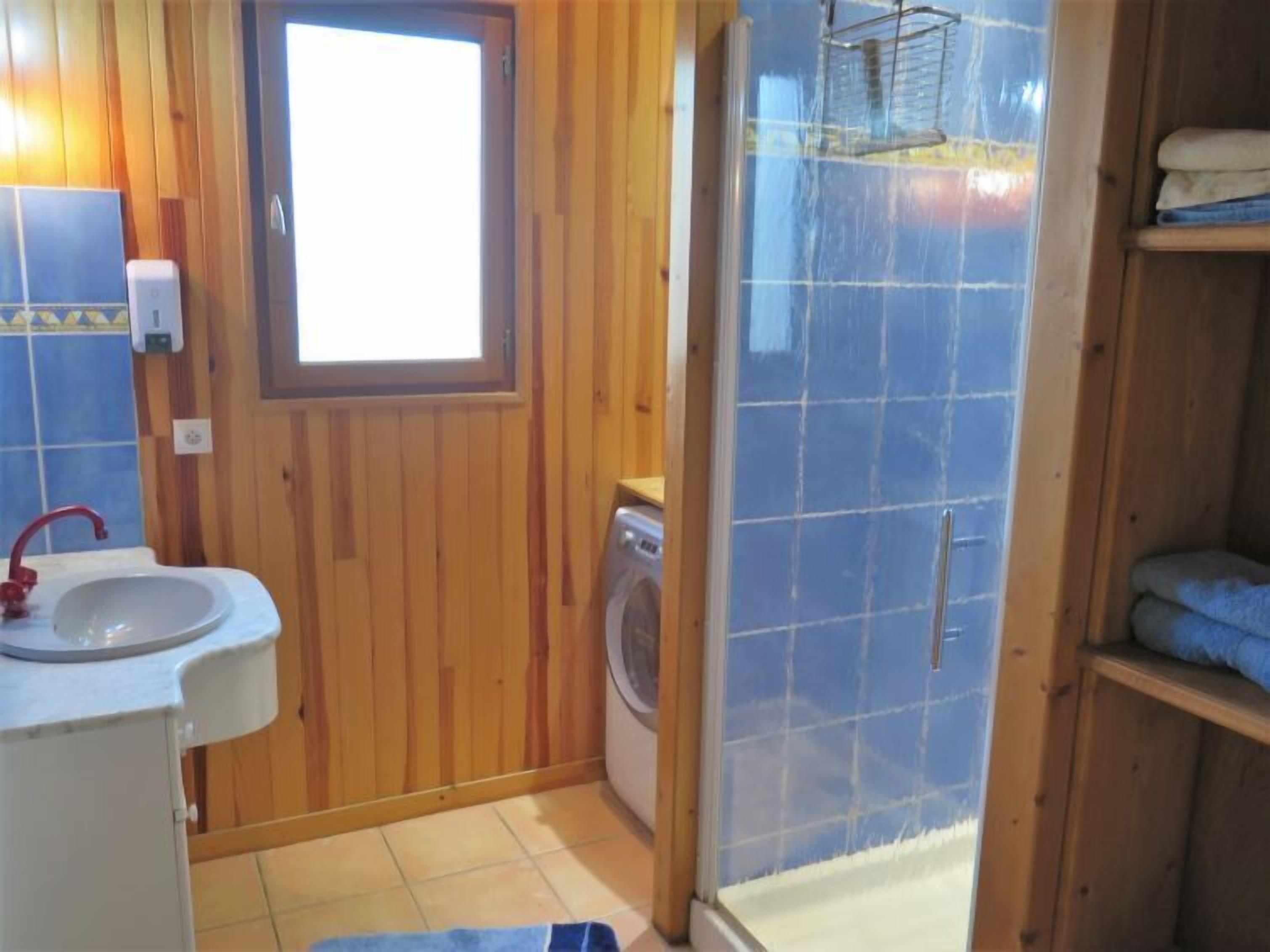 A small bathroom with wooden walls, a sink, a washing machine, and a shower area.