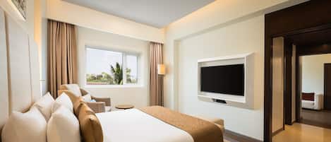 A hotel room with a large bed, a flat-screen TV, a window with curtains, and a view of palm trees.