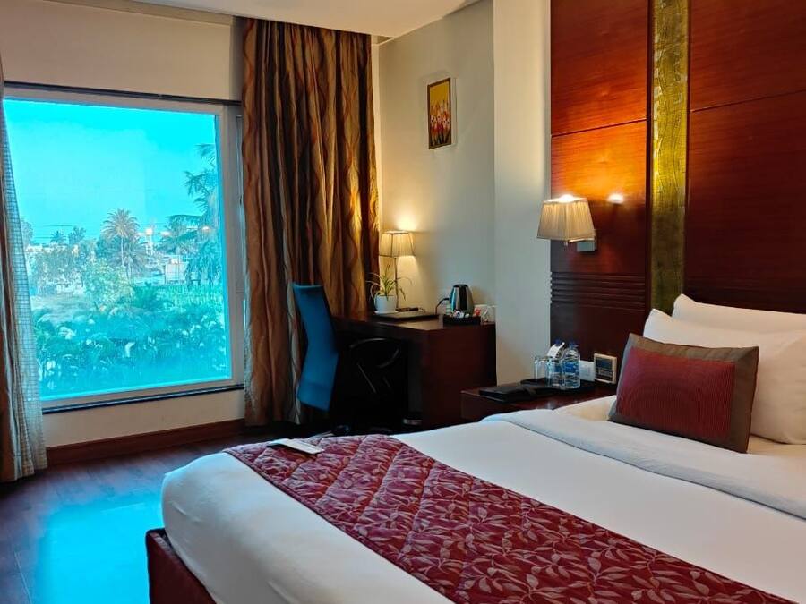 Habitación de hotel con una cama grande, un escritorio, una silla, una mesita de noche, una lámpara y vistas al exterior.