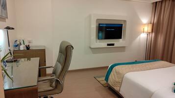 A hotel room with a bed, desk, chair, TV, and a lamp.