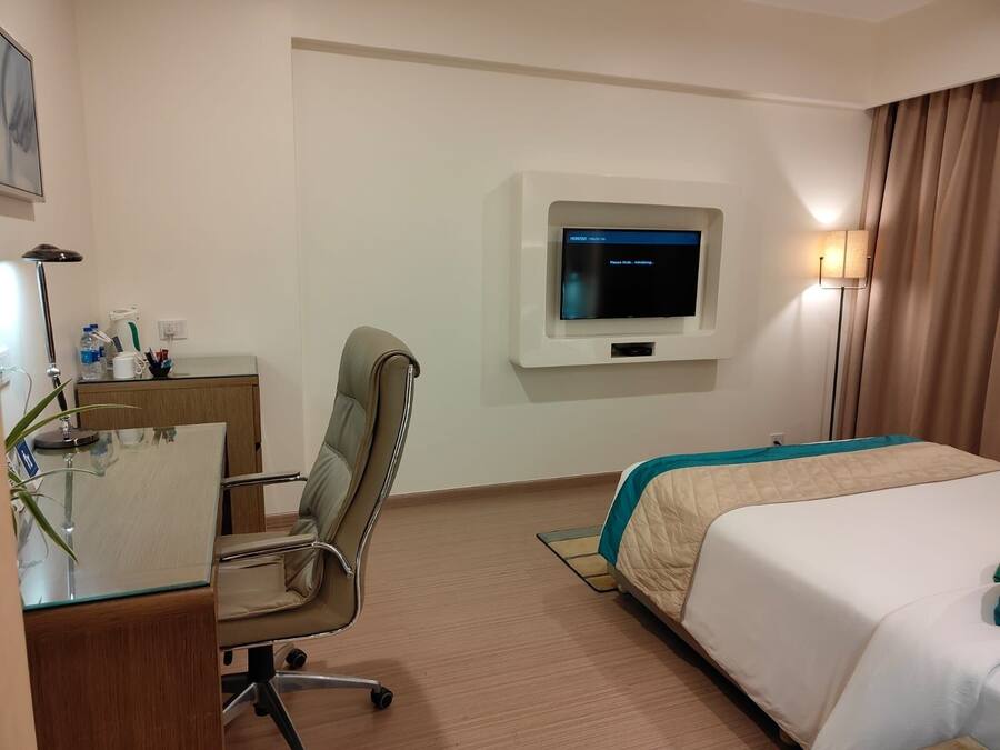 A hotel room with a bed, desk, chair, TV, and a lamp.