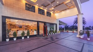 A hotel entrance with a reception desk, potted plants, and a covered outdoor area with palm trees. - Fortune Hosur  -  Member ITC Hotels' Group (Hosur)