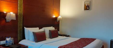 A hotel room with a large bed, two bedside tables, a nightstand, and a wall-mounted lamp.