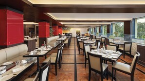 A spacious restaurant with high ceilings, multiple dining areas, and large windows offering views of the outdoors. - Fortune Hosur  -  Member ITC Hotels' Group (Hosur)
