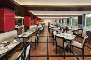 Un restaurante espacioso con techos altos, varias zonas de comedor y amplias ventanas que ofrecen vistas al exterior.