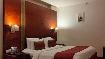 Habitación de hotel con una cama grande, cabecera de madera, dos lámparas de noche, una mesita de noche y una pequeña mesa con lámpara.