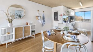 Una cocina moderna con armarios blancos, una zona de comedor con mesa redonda y vistas a la ciudad a través de grandes ventanales.
