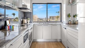 Cocina moderna con armarios blancos, un amplio ventanal con vista a la ciudad y una encimera con diversos objetos.