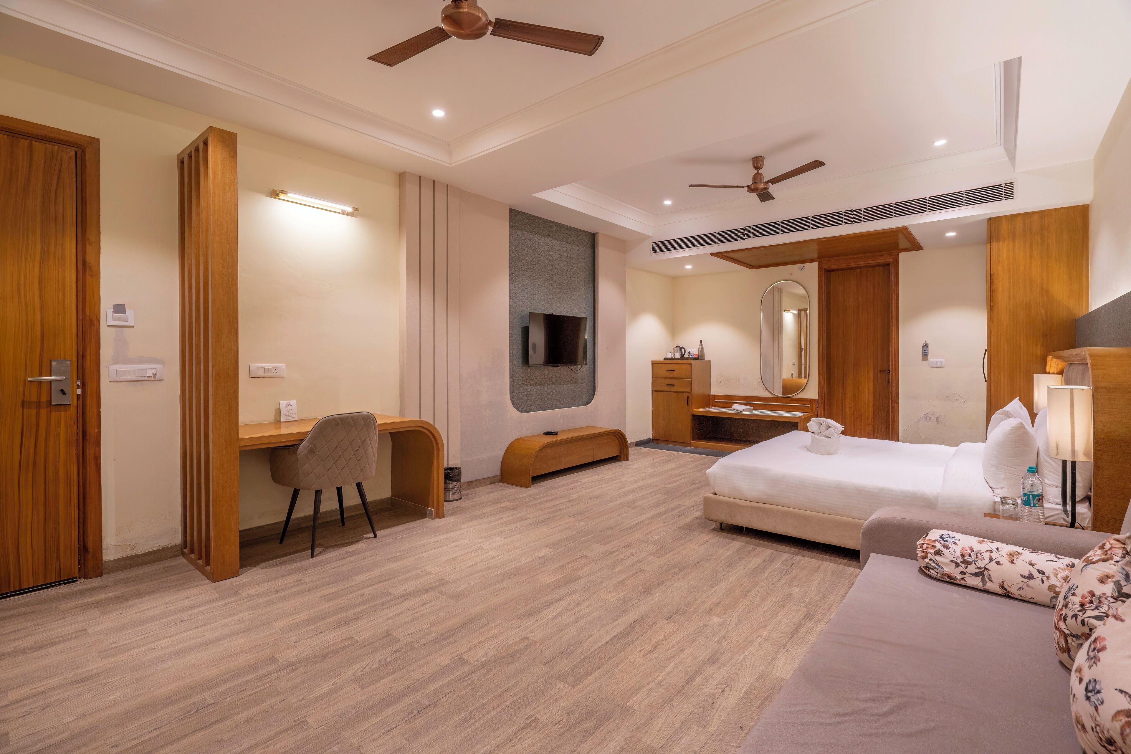 A modern hotel room with a wooden desk, a bed, a sofa, and a ceiling fan.