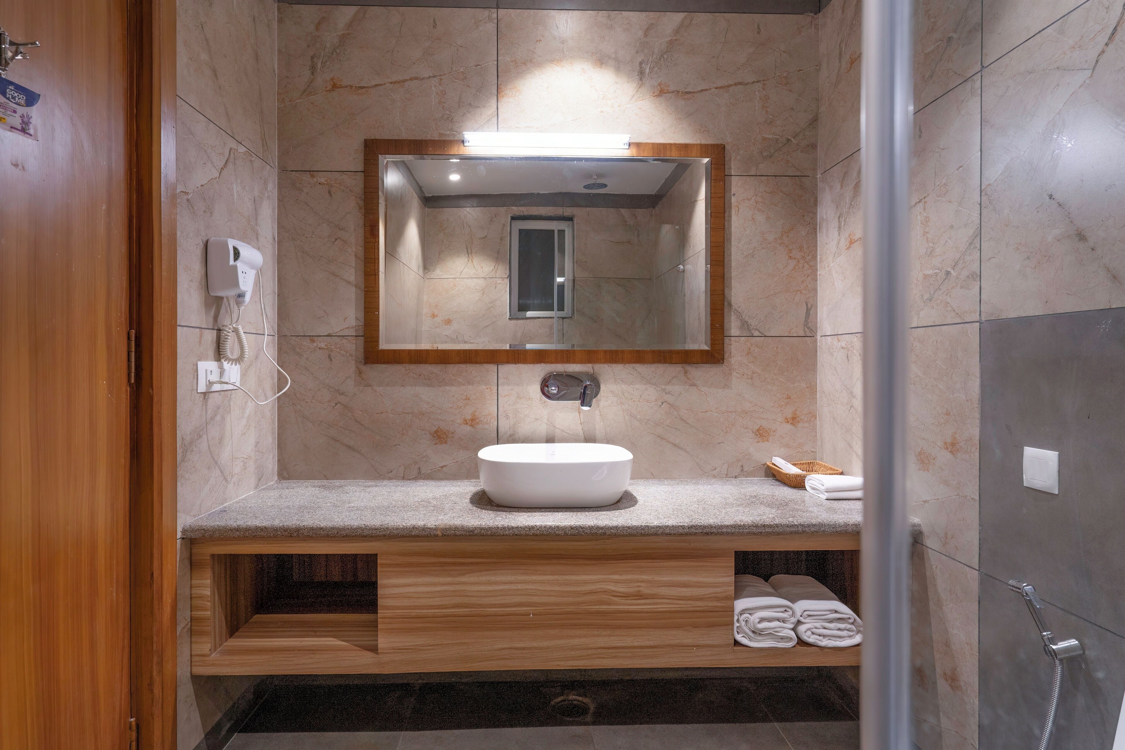 A modern bathroom with a marble wall, a wooden vanity, a sink, a mirror, and a shower.