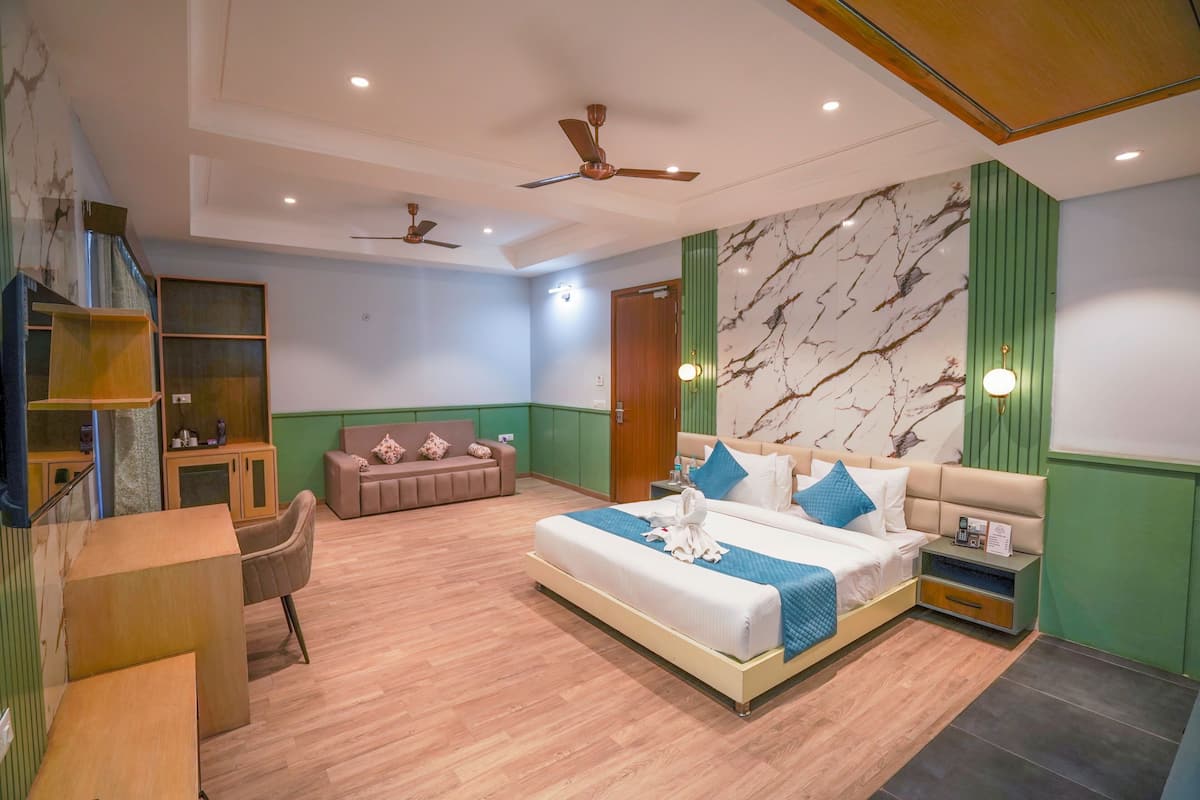 A modern hotel room with a large bed, a sofa, a desk, and a chair. There are ceiling fans, a marble wall, and a green accent wall.