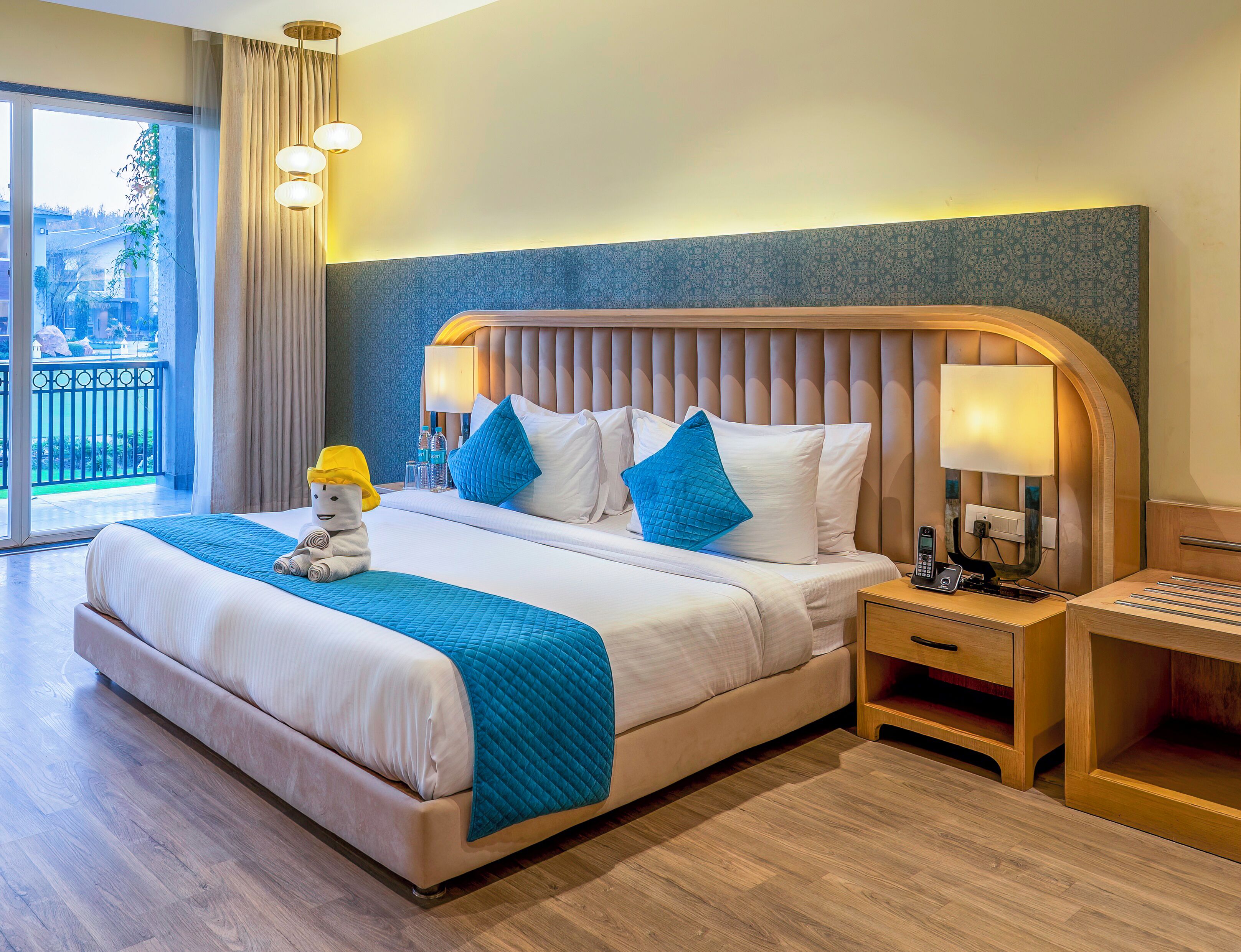 A hotel room with a large bed, two bedside tables, a nightstand, and a view of the outdoors.