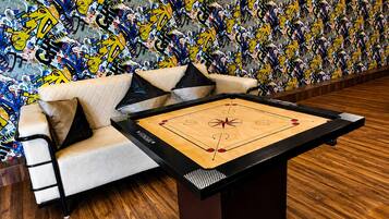 Et værelse med trægulv, en beige sofa med sorte og hvide puder, samt et shuffleboard-bord.