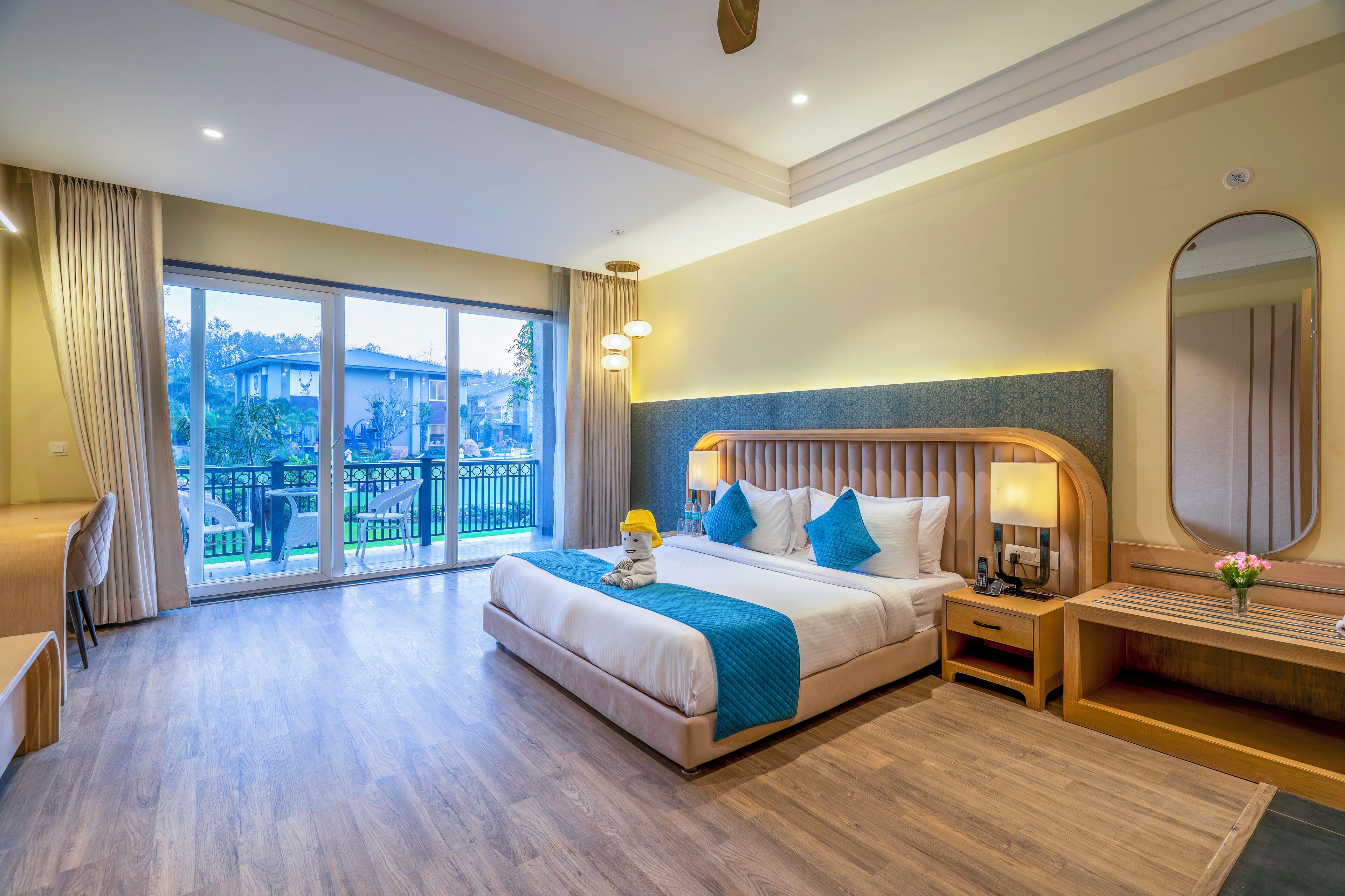 Habitación de hotel con una cama grande, cabecera de madera, mesita de noche, escritorio y vistas al exterior por una puerta corrediza.