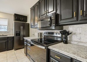 A modern kitchen with dark cabinetry, stainless steel appliances, and a herringbone tile backsplash. - Evergreen Luxe! Backyard Oasis w/ Hot Tub (Colorado Springs)