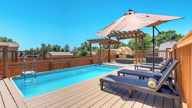 A wooden deck with a swimming pool, lounge chairs, and a pergola with an umbrella. - Evergreen Luxe! Backyard Oasis w/ Pool & Hot Tub! (Colorado Springs)
