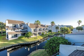 A modern residential building with a two-story layout, a covered patio, and a canal in front.