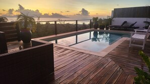 A wooden deck with a swimming pool, lounge chairs, and potted plants.