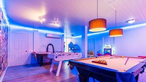 A room with a pool table, foosball table, air conditioning unit, and arcade games.