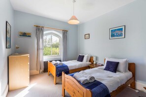 Una habitación con dos camas de madera, un escritorio de madera, una ventana con cortinas e imágenes enmarcadas en las paredes.