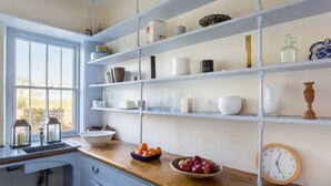 A kitchen with white cabinets, a wooden countertop, and a window with a view of a stone wall. - The Old Rectory with Swimming Pool (Bristol)