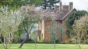 A brick house with a sloped roof and chimneys, surrounded by a well-maintained lawn and flowering trees. - The Old Rectory with Swimming Pool (Bristol)