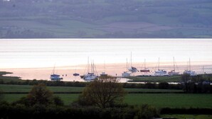 A coastal view with boats docked along the shore, a grassy foreground, and rolling hills in the background. - The Old Rectory with Swimming Pool (Bristol)