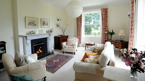 A traditional living room with a fireplace, comfortable seating, and a large window with curtains. - The Old Rectory with Swimming Pool (Bristol)
