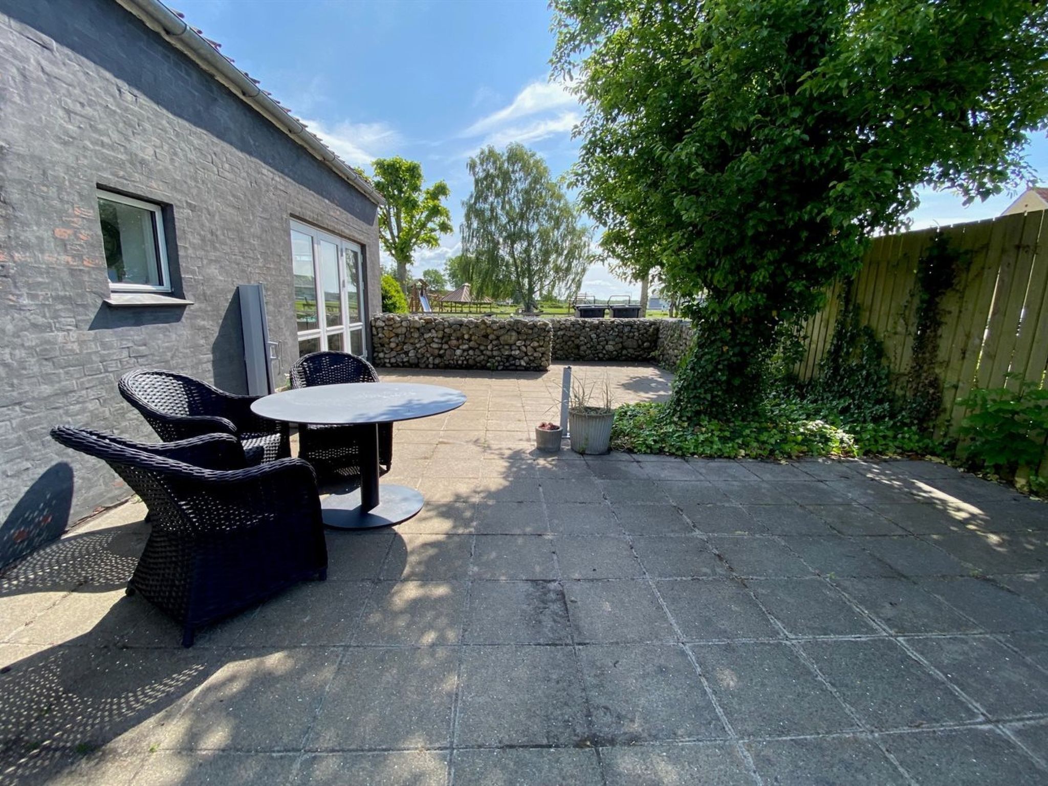 Une terrasse avec une table et des chaises, un mur en pierre et une clôture en bois.