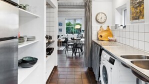 A modern kitchen with white cabinetry, a built-in washing machine, and a dining area with a view of greenery.