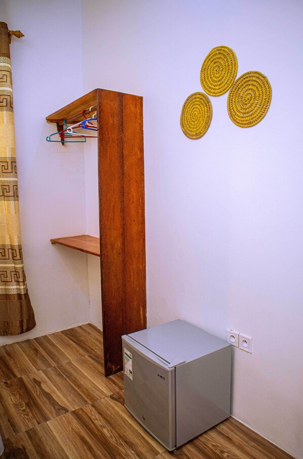 Una habitación pequeña con un armario de madera, un refrigerador pequeño y un estante en la pared con ropa.