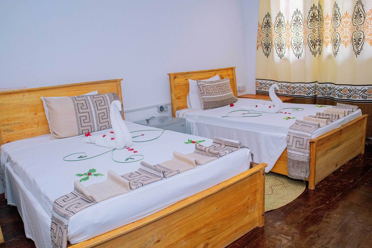 A hotel room with two wooden beds, each with a white bedspread and decorative pillows.