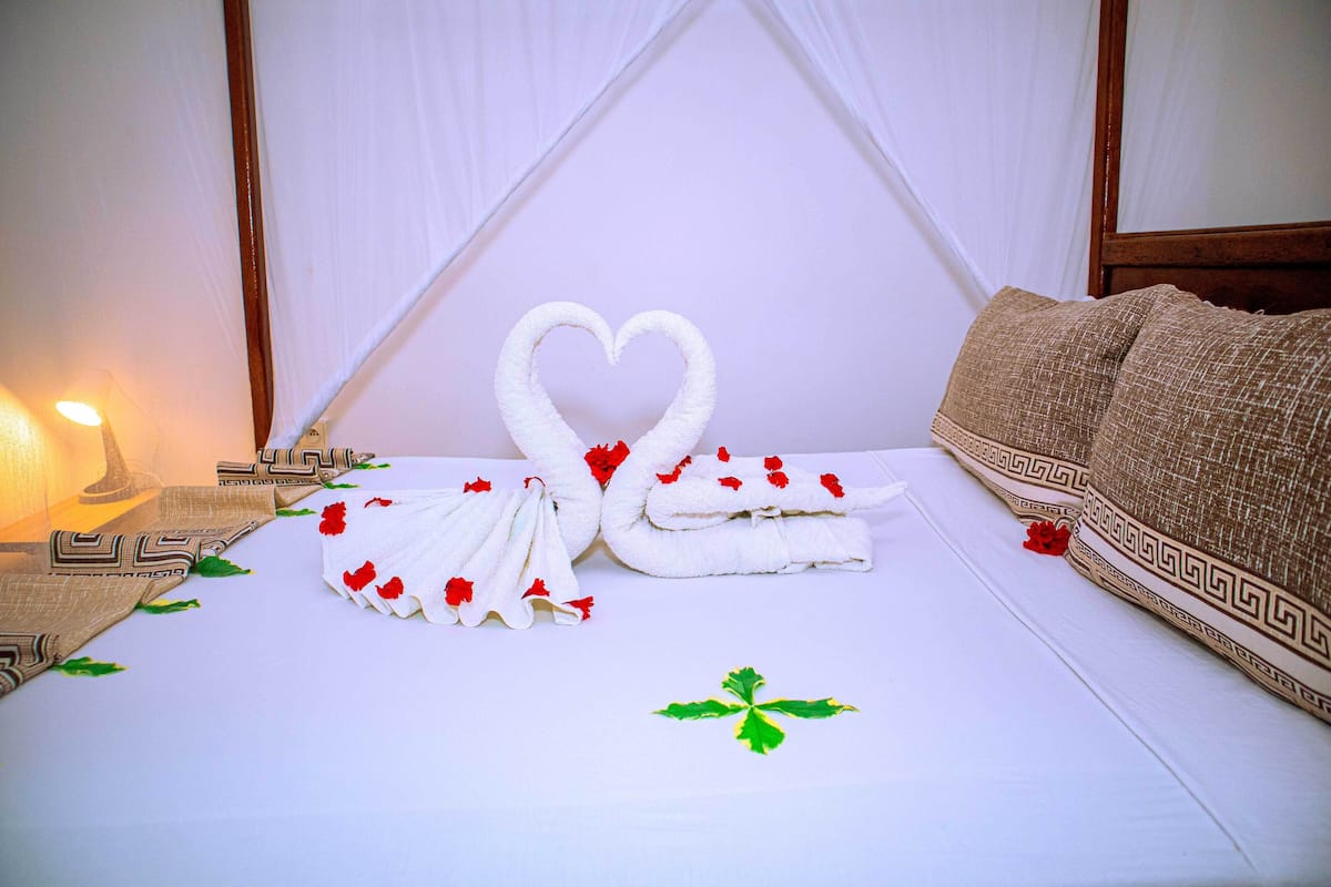 A bed with a white sheet, two towels shaped like swans, and red rose petals.