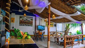Un restaurante con techo de paja, muebles de madera y una mesa con frutas y una carta.