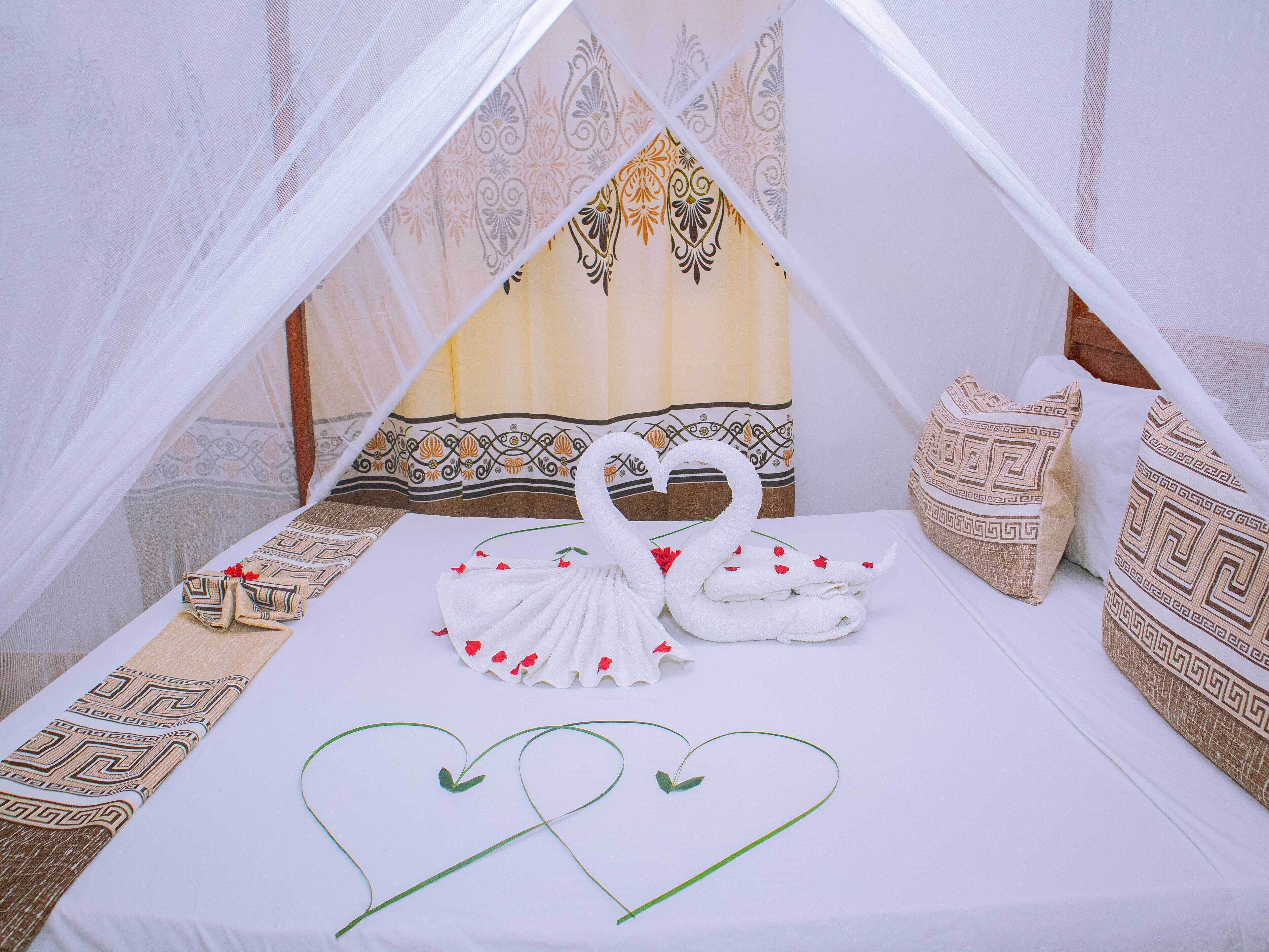 A bed with a canopy, decorative pillows, and a swan-shaped towel arrangement.