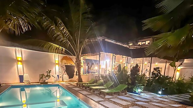 Una piscina con borde de guijarros, rodeada de sillas de descanso y palmeras.