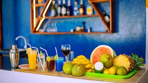 Una zona de bar con diversas bebidas, frutas y un coctelera sobre una mesa de madera.