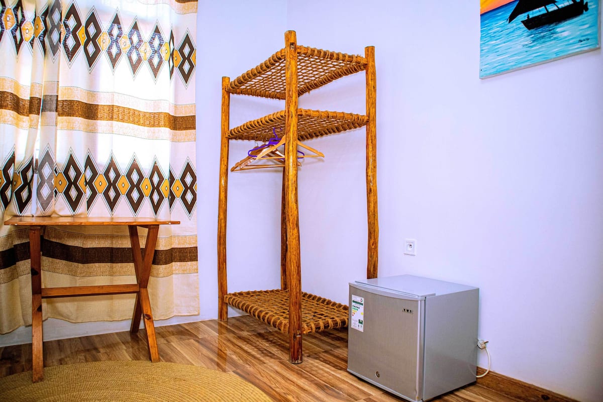 A room with a wooden bunk bed, a small refrigerator, and a table with a striped curtain.