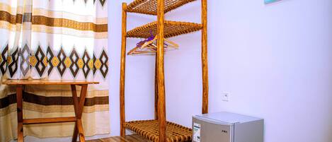 Une chambre avec un lit superposé en bois, un petit réfrigérateur et une table surmontée d’un rideau à rayures.