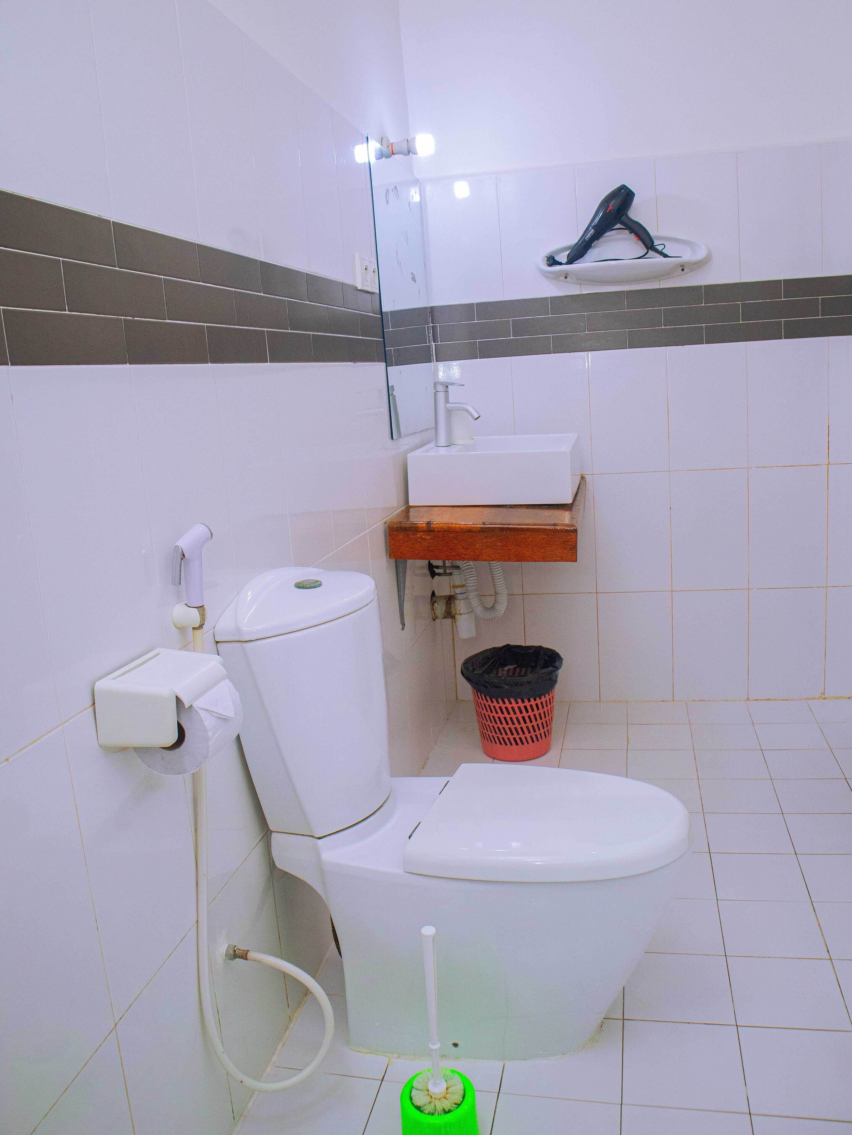 A bathroom with a toilet, sink, and a hand dryer on a shelf.
