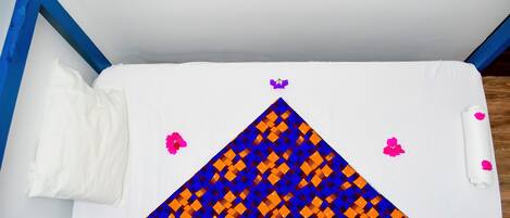 A small, white, single-bed room with a blue frame, a patterned bedspread, and pink flowers on the bed.