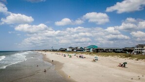 A beach with houses in the background, a clear sky, and people on the sand.