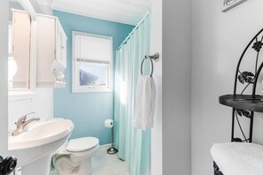 A bathroom with a white sink, toilet, and a shower area with a curtain. - Amazing Dog Friendly Oceanfront 3 Bedroom Cottage, Steps to the Beach (Oak Island)