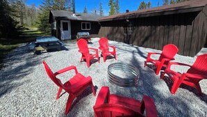 Une cabane en bois avec un patio en gravier, des chaises Adirondack rouges et un barbecue.