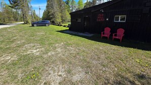 Un bâtiment rustique portant l’inscription « Old Mill Camp », avec une cour verdoyante et deux chaises Adirondack rouges.