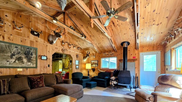 L’intérieur chaleureux d’un chalet avec des murs en bois, une cheminée, un ventilateur de plafond et différentes têtes d’animaux montées au mur.