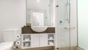 A modern bathroom with a white toilet, a large sink, and a glass shower enclosure. - Spa Suite Beach Club 3221 (Cairns)